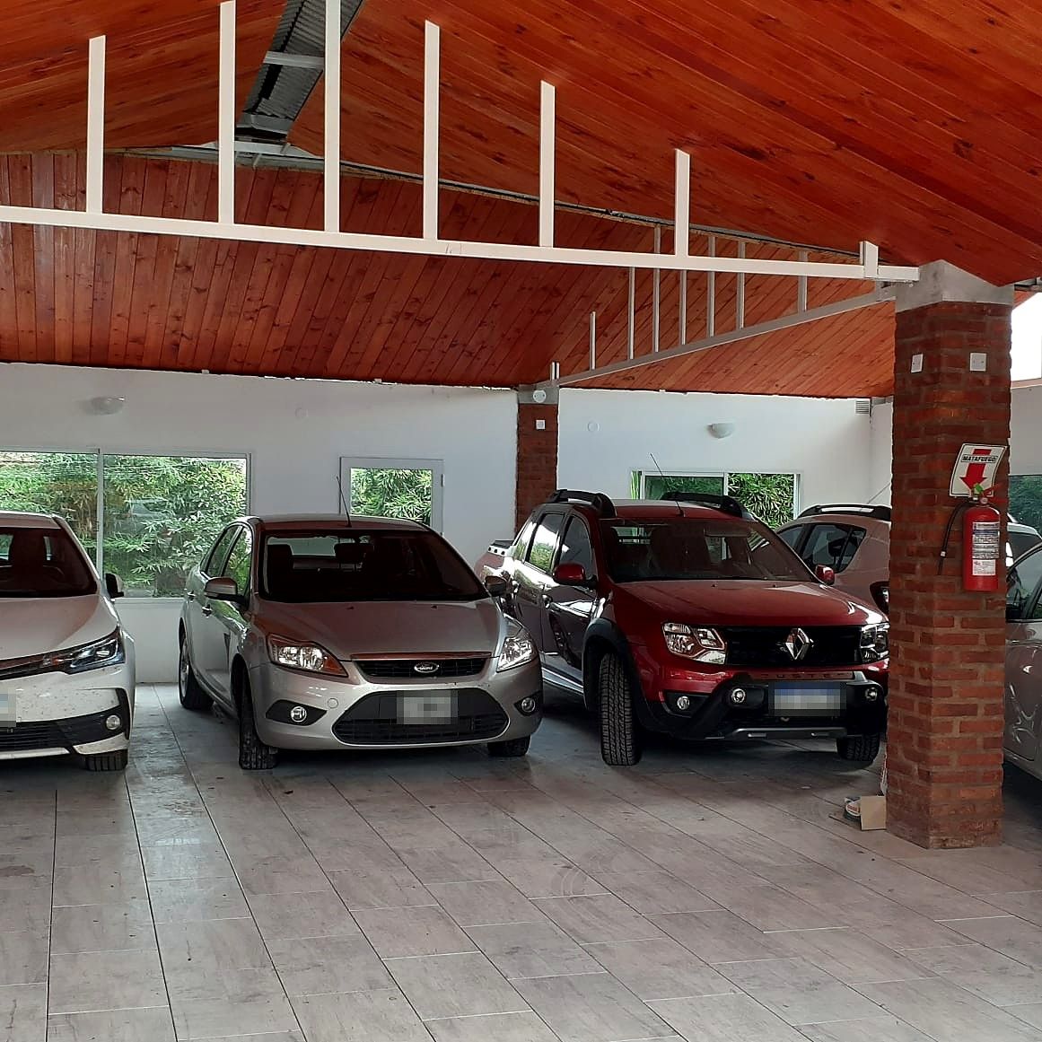 Autos en la cochera cubierta, junto a una columna de ladrillo con matafuegos