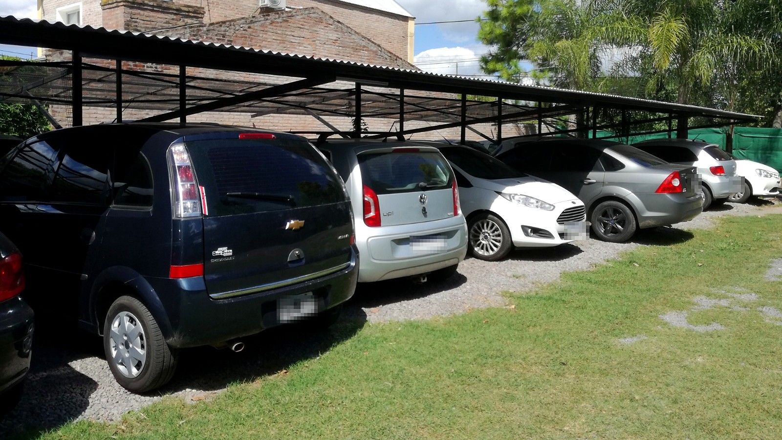 Fila de autos bajo el tinglado, en el parque del predio